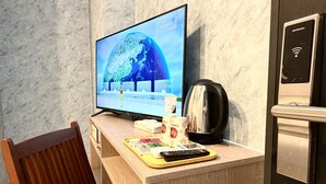 Une chambre d’hôtel avec un bureau en bois, un téléviseur affichant les prévisions météorologiques, une machine à café et une télécommande.