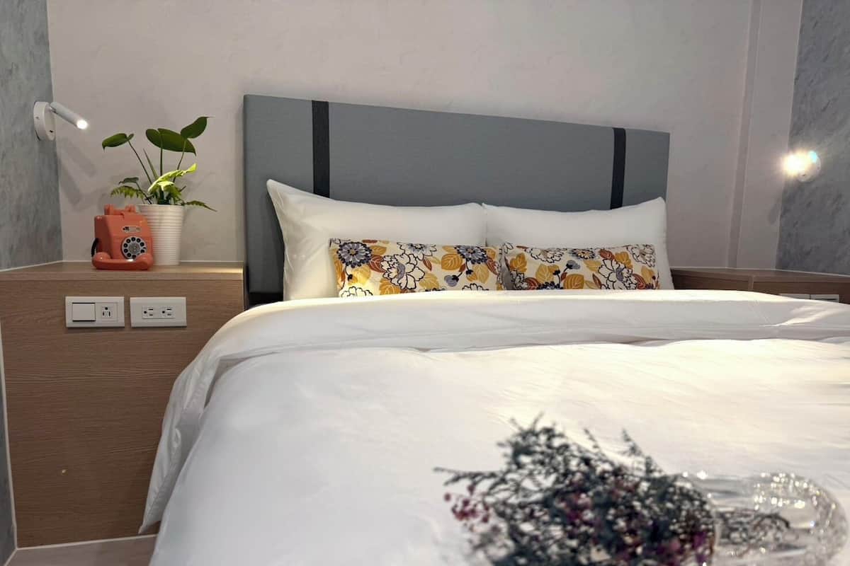 Une chambre d’hôtel moderne équipée d’un lit, d’une table de chevet, d’une lampe fixée au mur et d’une plante en pot.