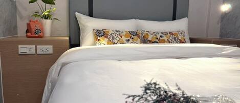 A modern hotel room with a bed, bedside table, wall-mounted lamp, and a potted plant.