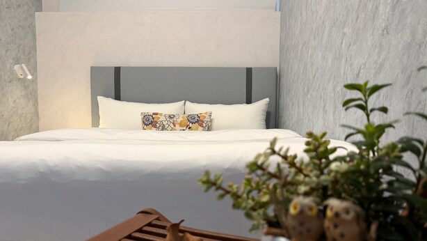 Une chambre à coucher moderne avec un grand lit, une tête de lit, une table de chevet agrémentée d’une plante et un banc en bois.