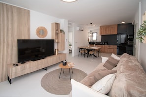 A modern living room with a flat-screen TV, a wooden entertainment unit, a round coffee table, and a beige sofa. - Luxury apartment with roof terrace (San Miguel de Salinas)