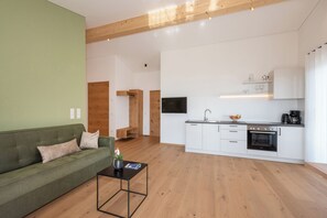 Ein modernes Wohnzimmer mit einem grünen Sofa, einem Couchtisch und einer Küche mit weißen Schränken sowie einem Einbauofen.