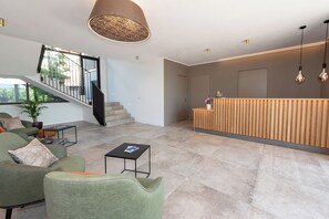 Ein moderner Empfangsbereich mit einem Holzbüro, einer Treppe und einer grünen Sitzgruppe mit einem Couchtisch.