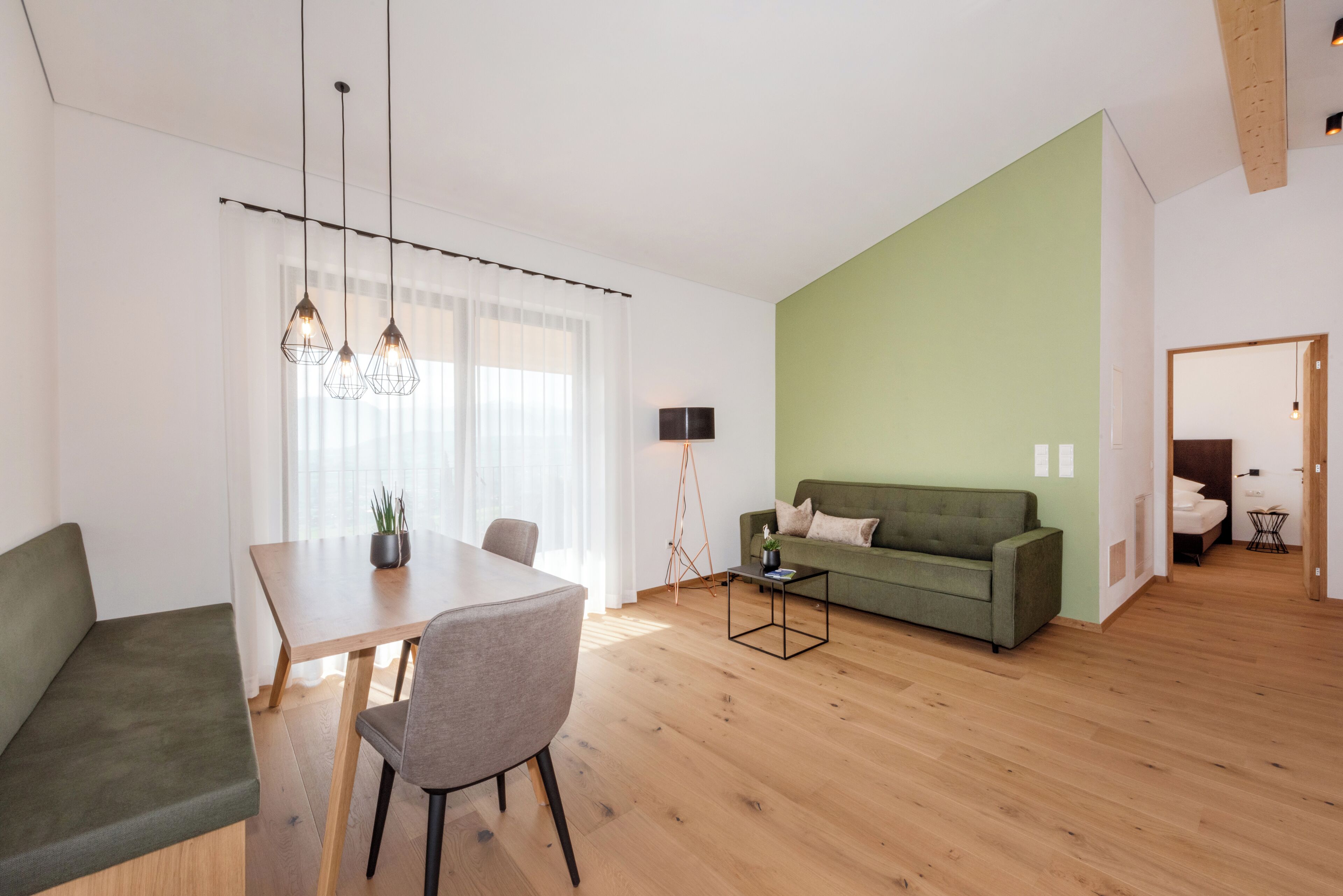 A modern living room with a dining area, a green sofa, and a wooden floor.