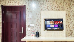 Ein Hotelzimmer mit Holztür, integriertem Fernseher auf einer Holzauslage und einem kleinen Tisch mit Flasche und Tasse.