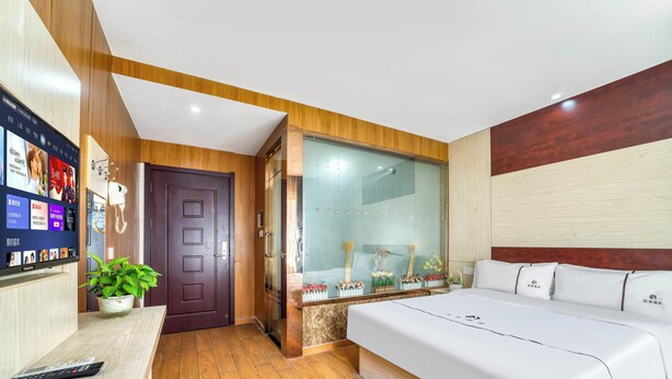 Ein modernes Hotelzimmer mit einem großen Bett, einem Schreibtisch mit Computer, einer Topfpflanze und einer Glassturzwand.