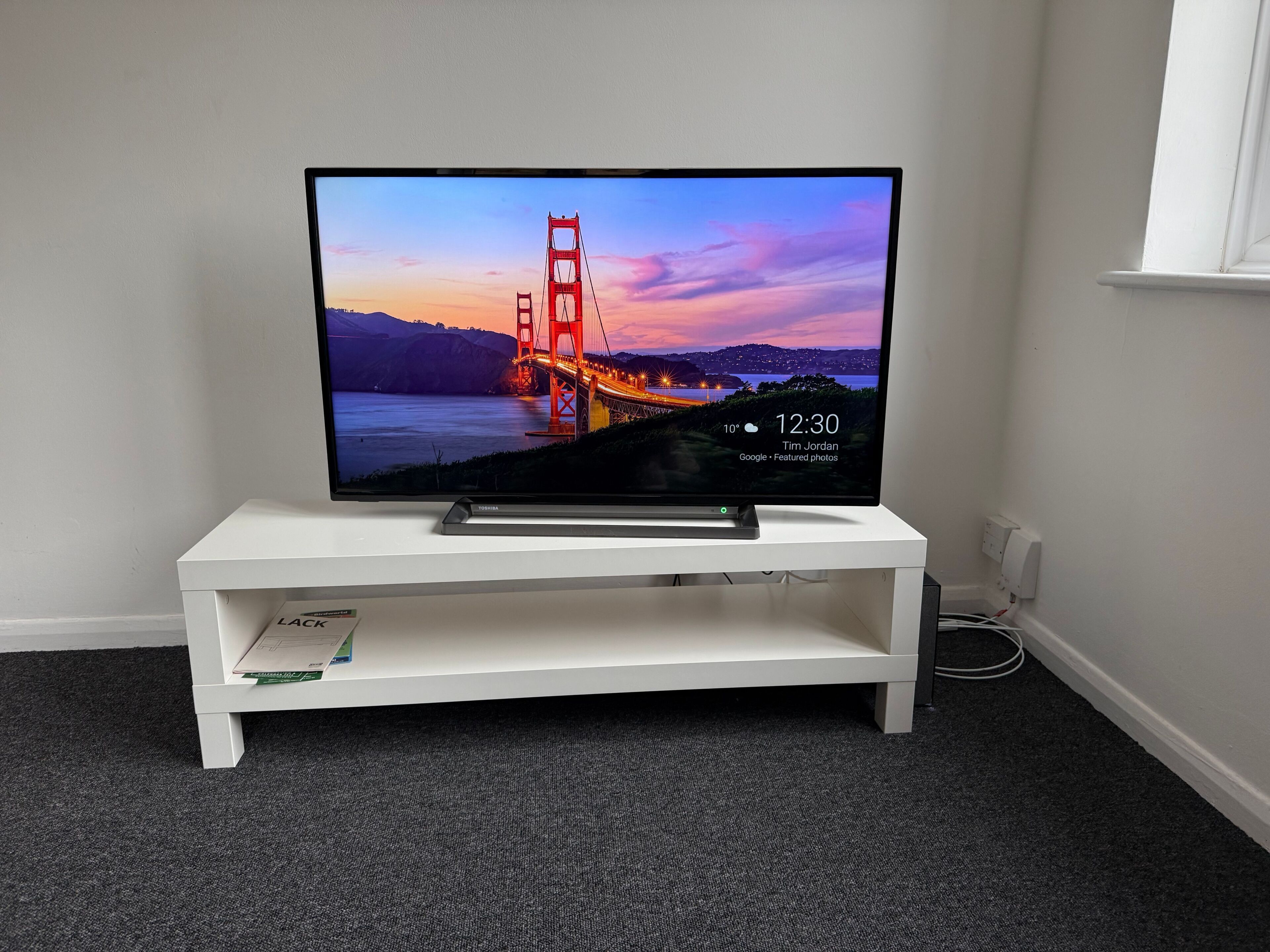 A flat-screen TV on a white TV stand in a room with carpeted flooring.