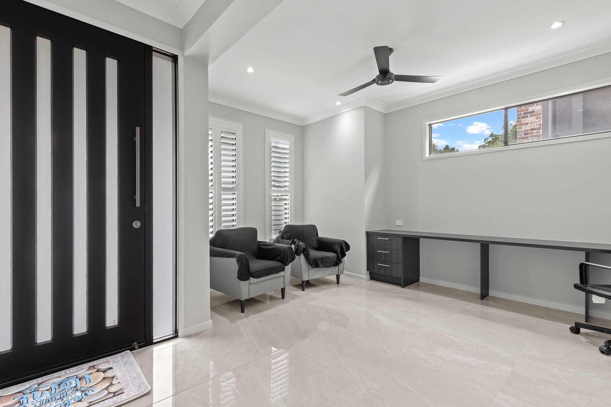 A modern, well-lit room with a ceiling fan, a large window with a view, and a desk with drawers.