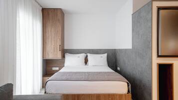 Un dormitorio moderno con cabecera de madera, cama con ropa de cama blanca, sofá gris y un espejo grande.