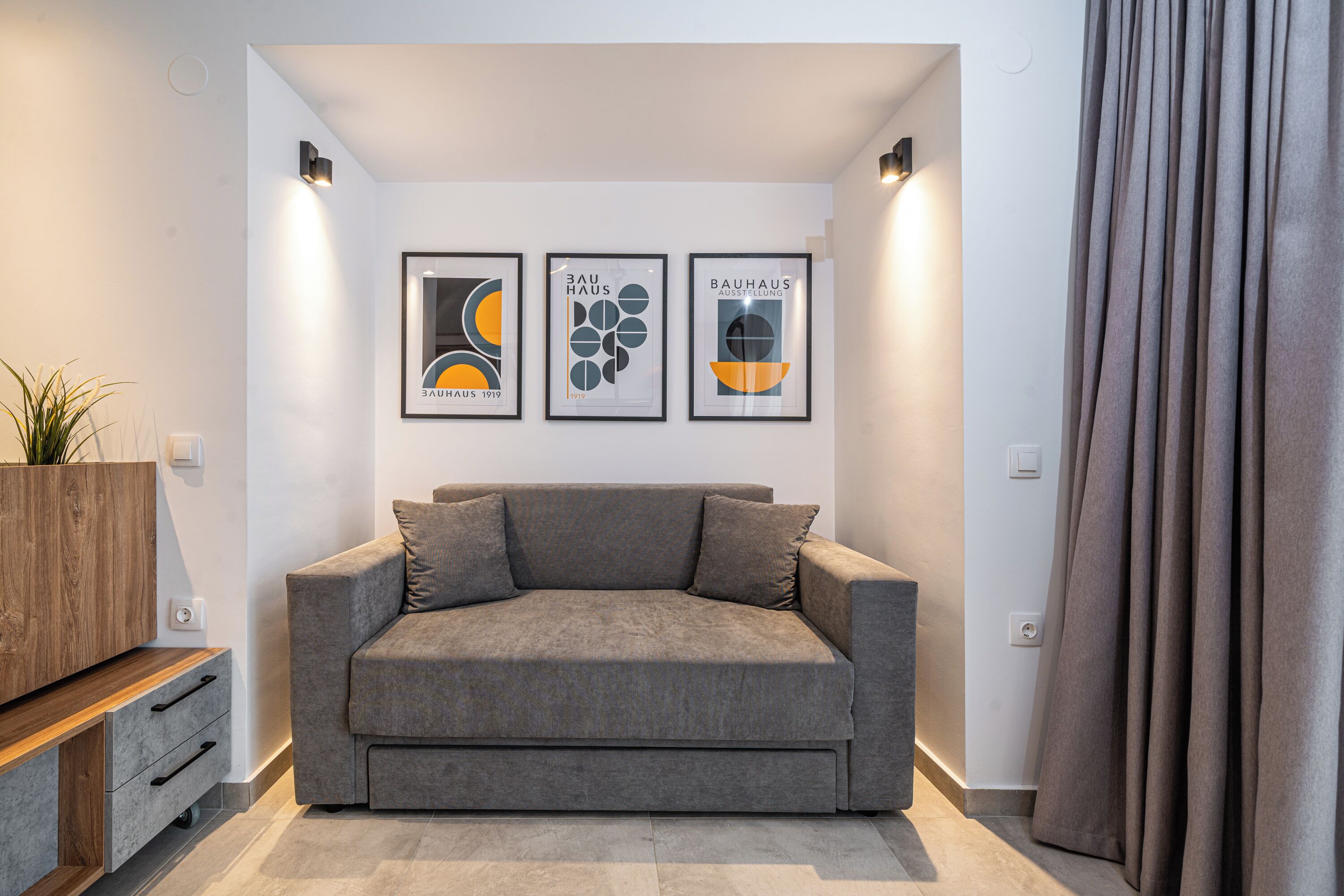 Uma sala de estar moderna com um sofá cinzento, um aparador de madeira e três quadros abstratos na parede.
