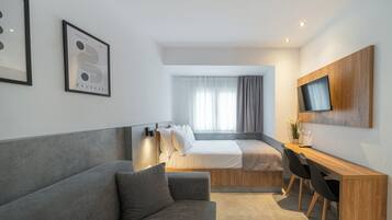 Una habitación de hotel moderna con un sofá gris, un escritorio de madera, una cama y un televisor instalado en la pared.