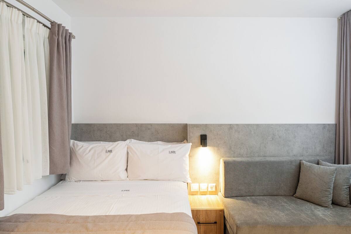 A hotel room with a bed, a sofa, a nightstand with a lamp, and curtains.