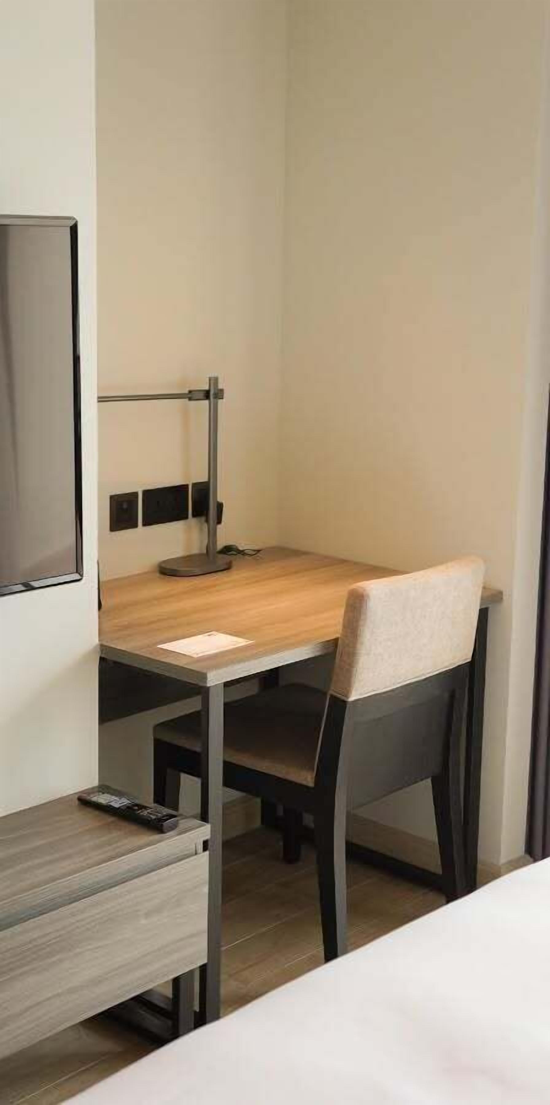 A hotel room with a bed, a desk with a chair, a television, and a bedside table.