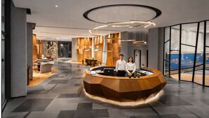 Un hall d’hôtel moderne doté d’un comptoir d’accueil central, d’un vaste espace salon et d’une grande fenêtre offrant une vue sur l’intérieur.