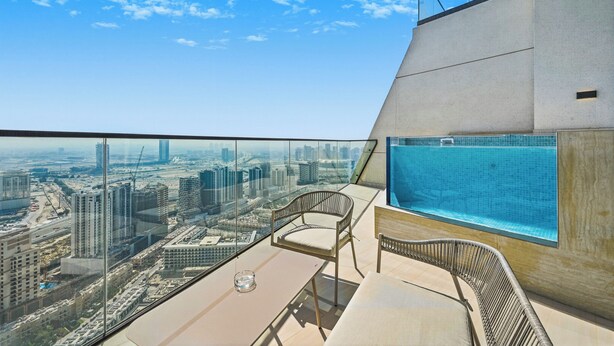 A high-rise balcony with a city view, a pool, and modern seating. - Bloomfields Iconic 1BR Binghatti Phanto (Dubai)