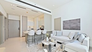 A modern living room with a white sofa, a coffee table, and a dining area with bar stools. - Bloomfields Iconic 1BR Binghatti Phanto (Dubai)