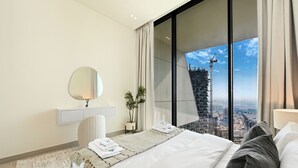 A hotel room with a large bed, a bedside table with a lamp, a mirror, and a view of a cityscape through a large window. - Bloomfields Iconic 1BR Binghatti Phanto (Dubai)