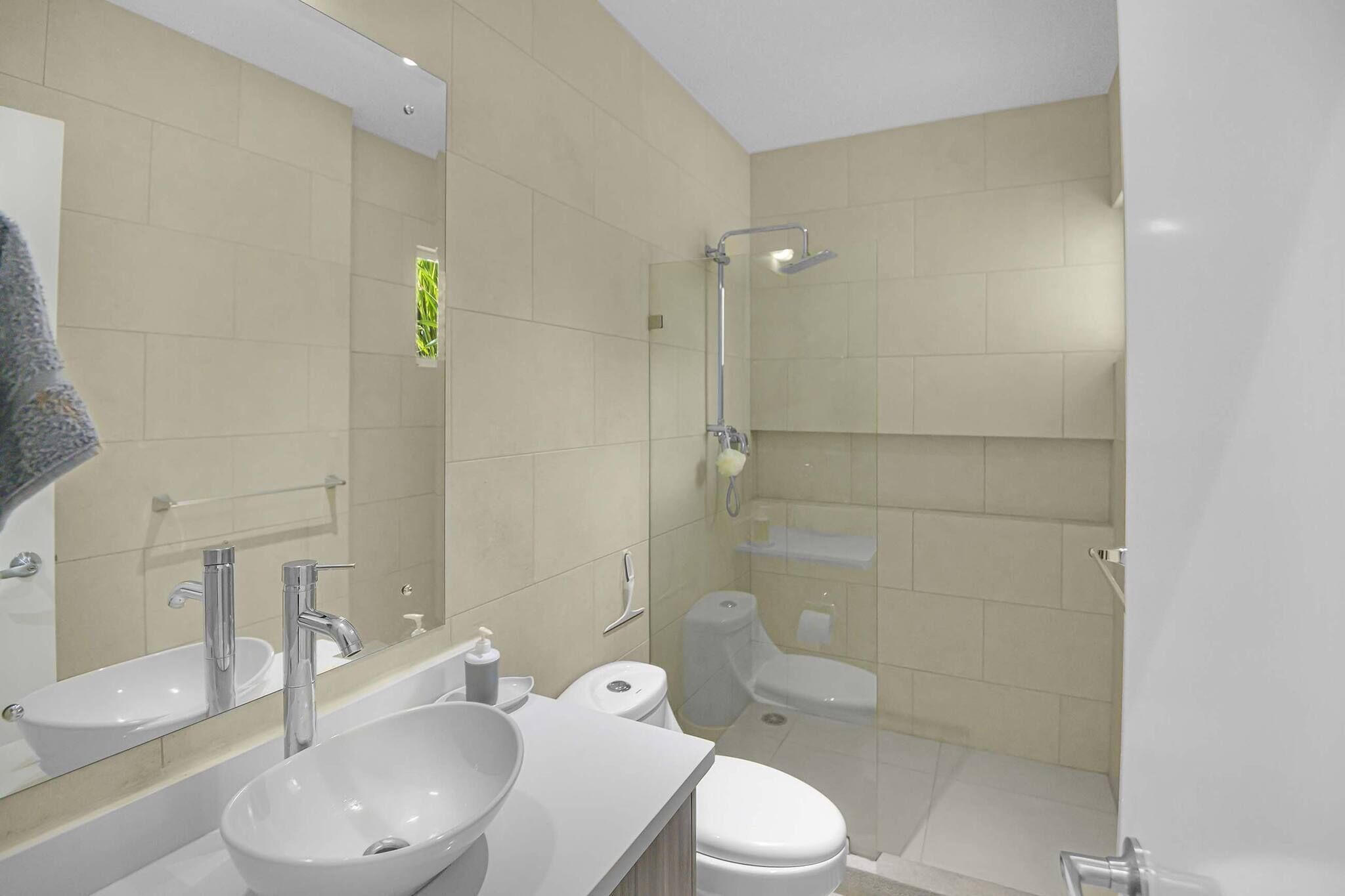 A modern bathroom with a large mirror, two sinks, a toilet, and a shower.