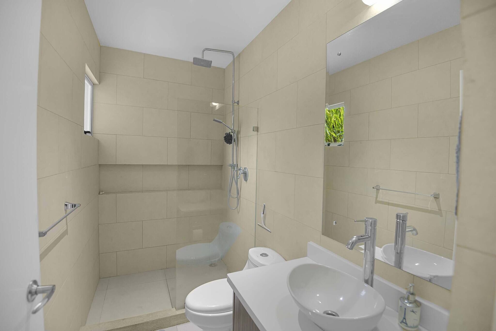 A modern bathroom with a shower, toilet, sink, and mirror.