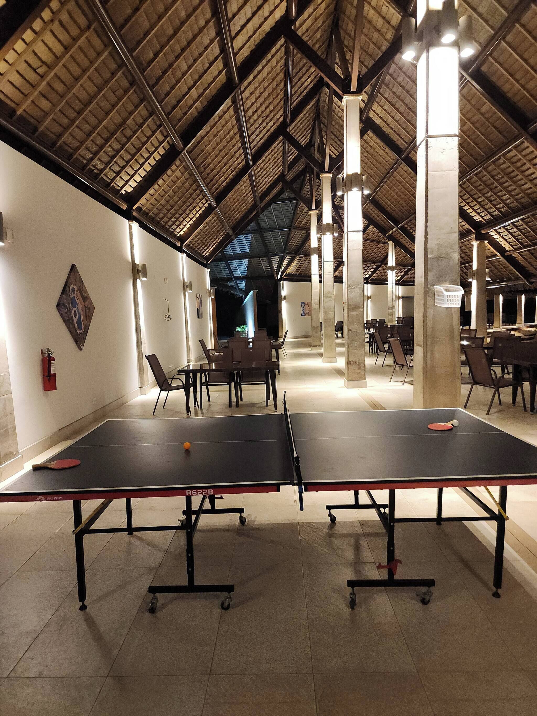 A spacious indoor area with ping pong tables, chairs, and a high ceiling with exposed beams.