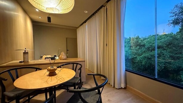 Een moderne eetruimte met een ronde tafel en stoelen, een hanglamp en uitzicht op groen door grote ramen.