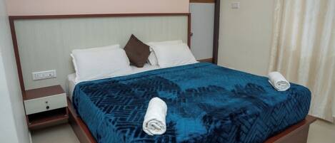 Una habitación de hotel estándar con cama, mesita de noche y cortina.