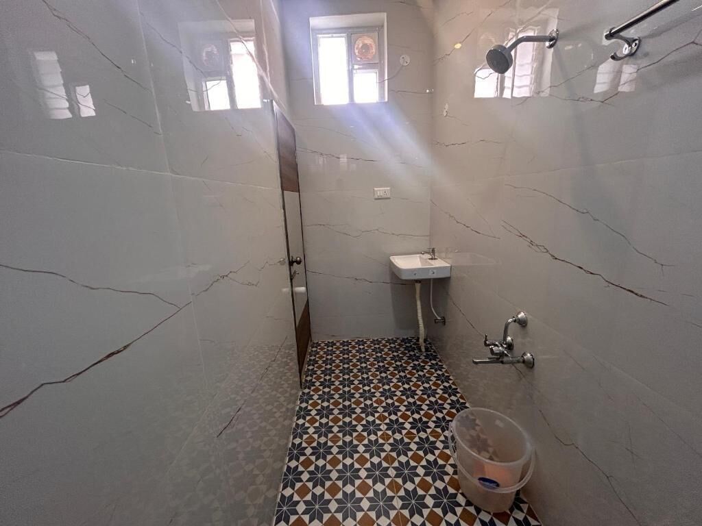 Een kleine badkamer met betegelde vloer, een wastafel en een douchehoek.