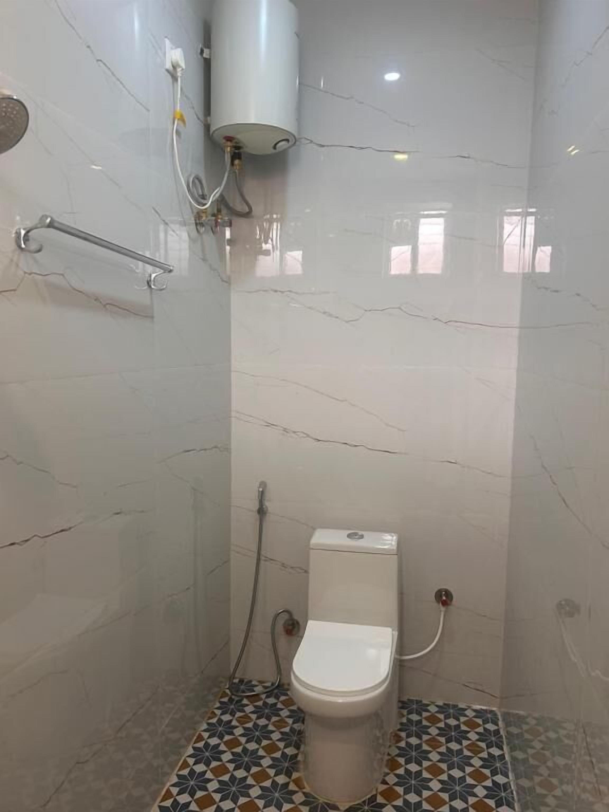 Et lille, kompakt badeværelse med toilet, bruser og gelænder.