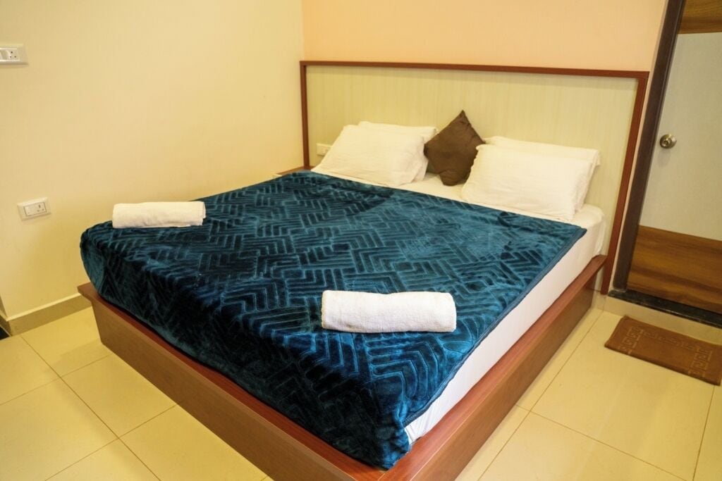 A neatly made bed with a patterned bedspread and two pillows, a wooden headboard, and a tiled floor.