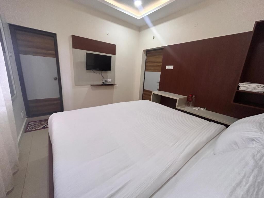 Een hotelkamer met een bed, een aan de muur bevestigde televisie, een spiegel en een plank met handdoeken.