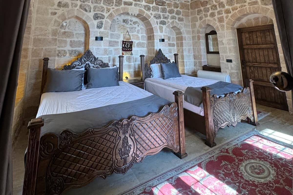 Habitación con paredes de piedra, dos camas, una lámpara colgante y una alfombra estampada.