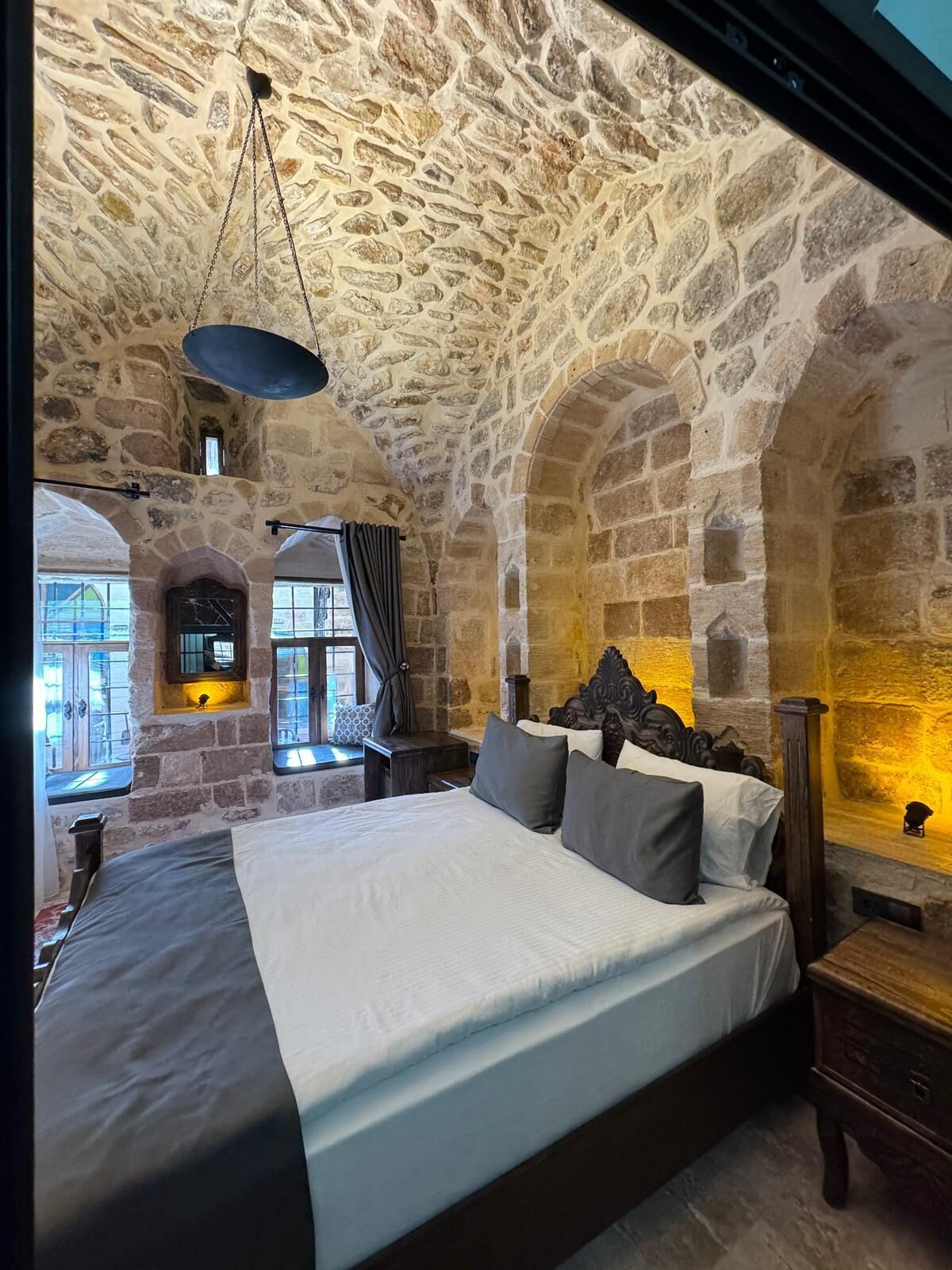 A stone-walled bedroom with a large bed, a wooden headboard, and a stone fireplace.
