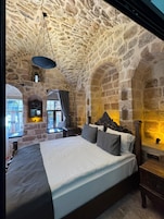 A stone-walled bedroom with a large bed, a wooden headboard, and a stone fireplace.
