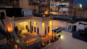 A courtyard with a staircase, outdoor seating, and a building with arches. - Sila Konagi Hotel (Mardin)