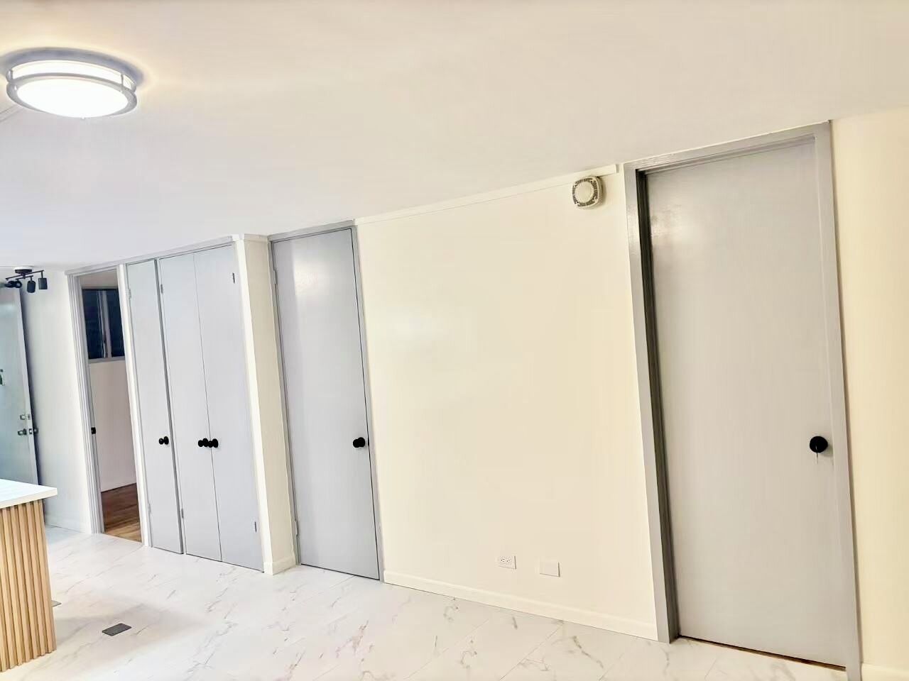 Una habitació amb parets blanques, un paviment de marbre i diverses portes blanques amb nassos negres.