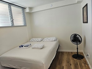 Ein Schlafzimmer mit einem Bett, Kissen, einem Ventilator und einem Fenster.