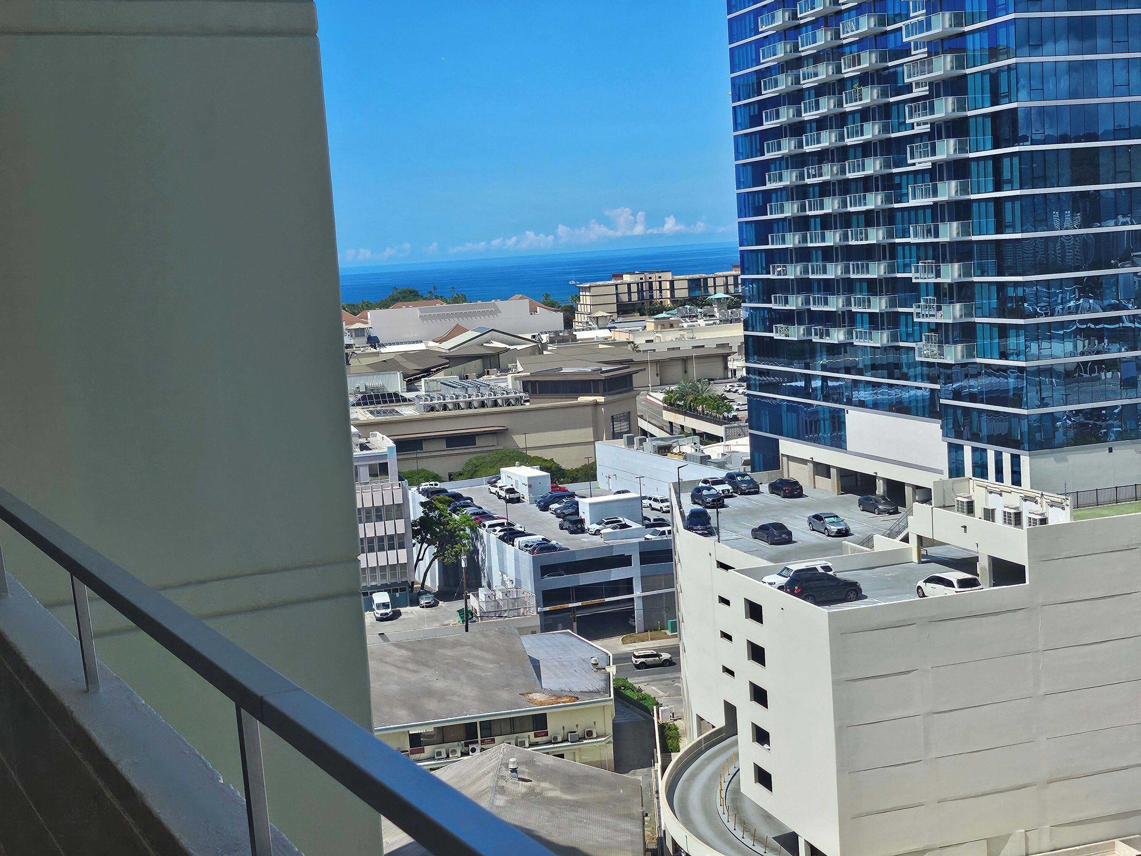 A high-rise building with a view of the ocean and a parking area with several cars.