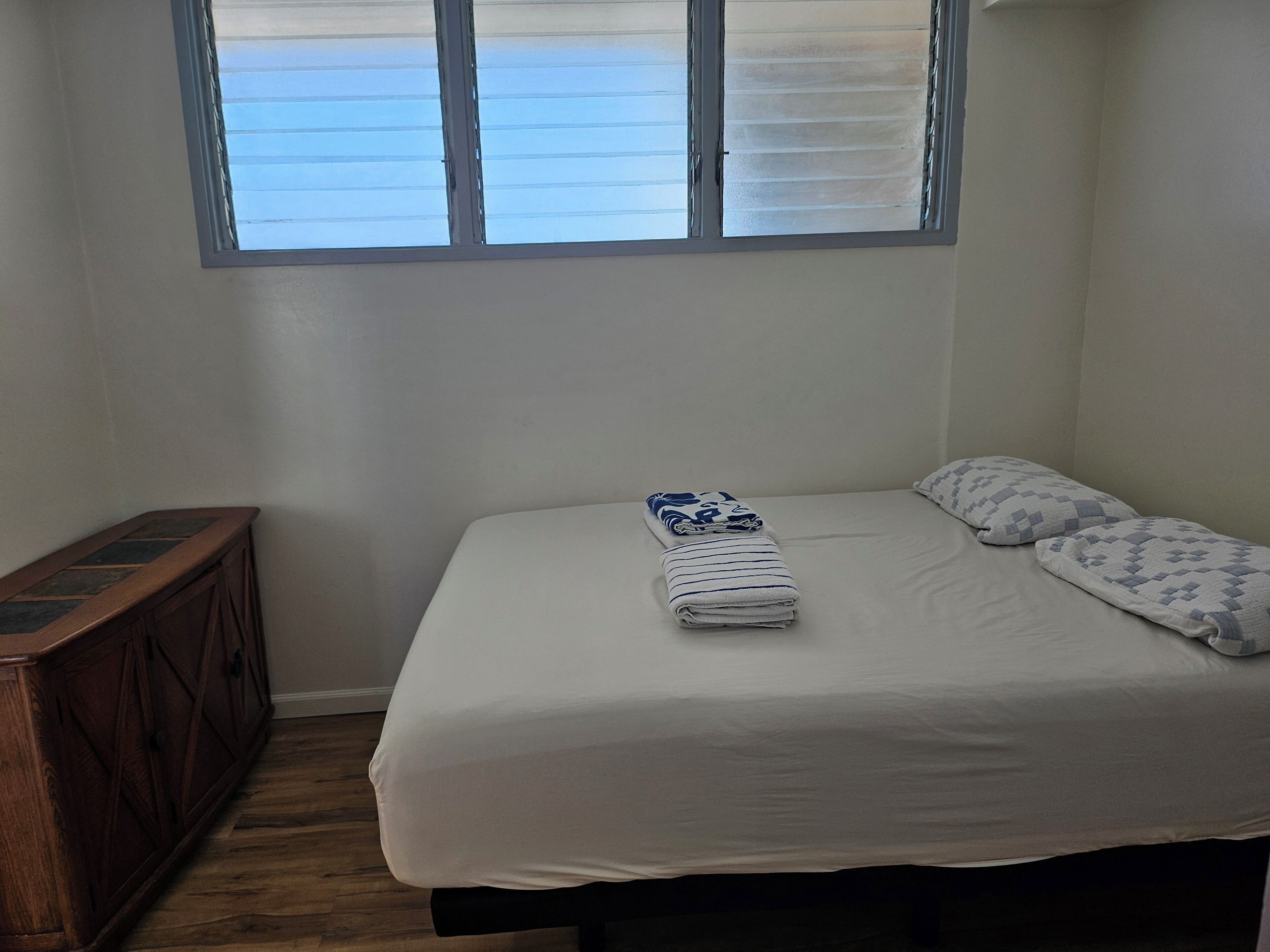 Un dormitorio con cama, almohadas, una toalla doblada y una ventana con persianas.
