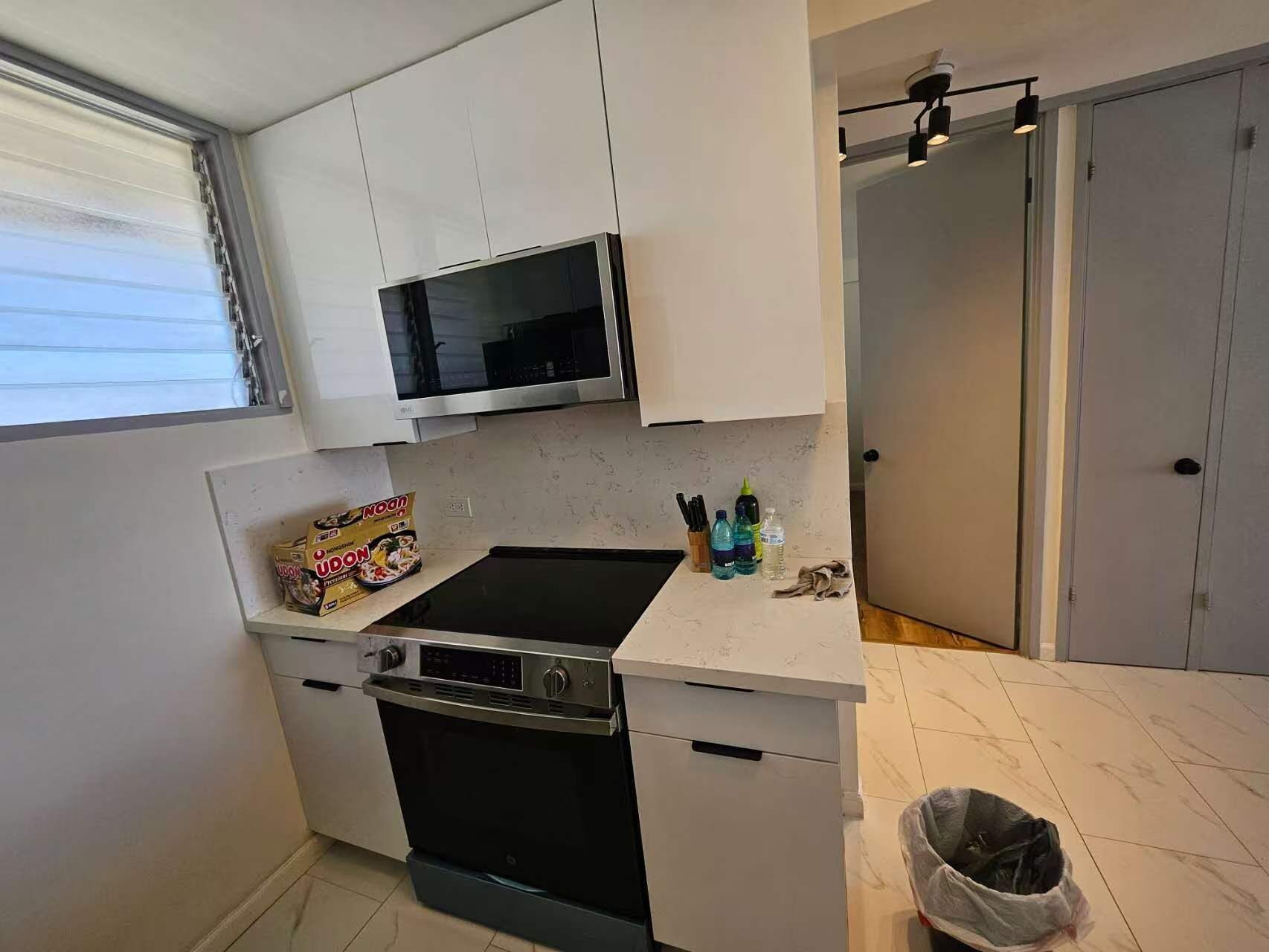 Une cuisine compacte avec des meubles blancs, un four à micro-ondes, une cuisinière et un petit plan de travail.