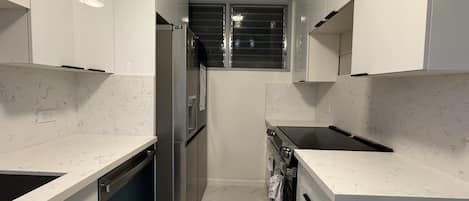 Une cuisine moderne avec des meubles blancs, des appareils en acier inoxydable et une fenêtre équipée de stores.