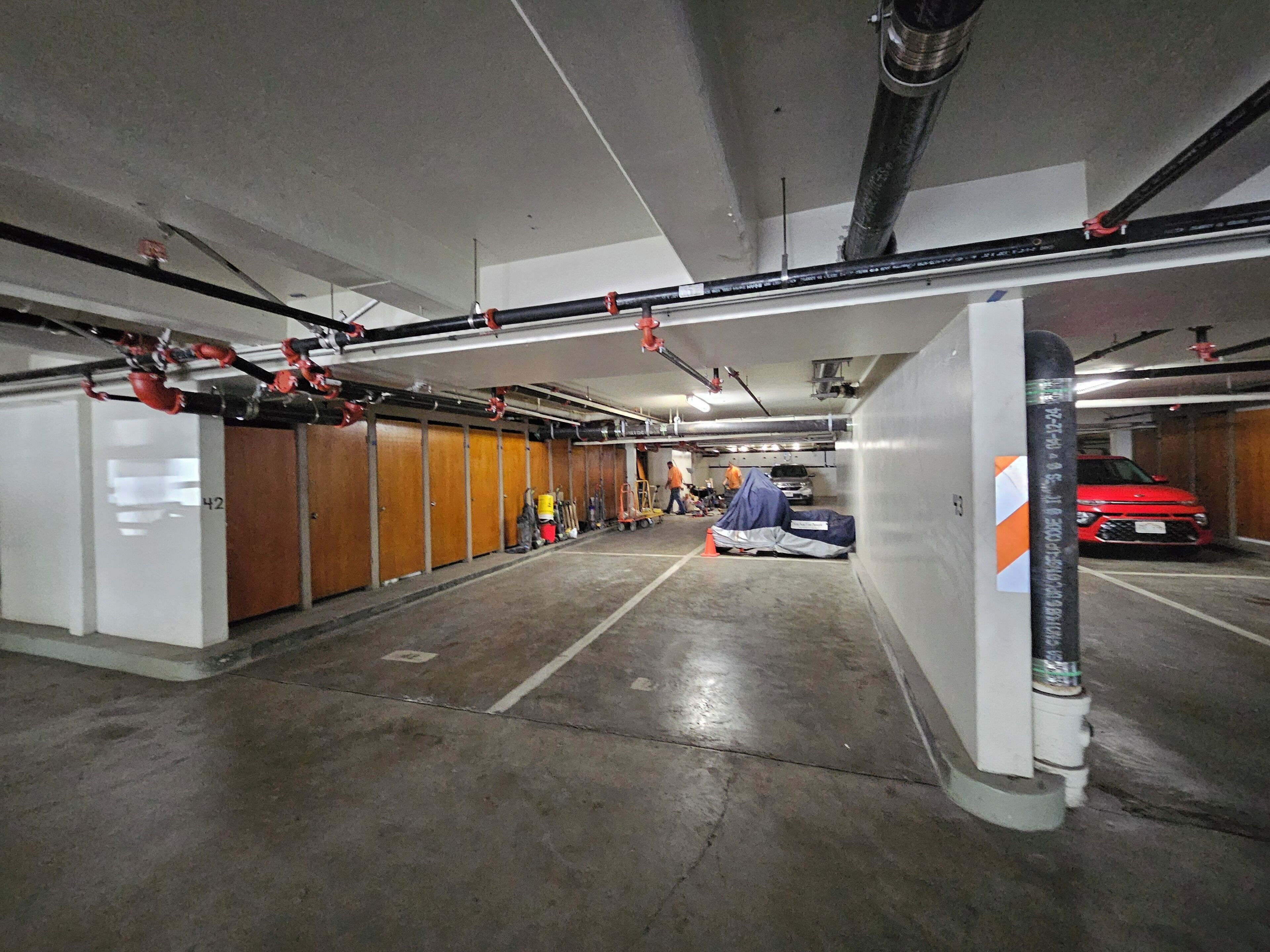 Un estacionamiento de varios niveles con pisos de concreto, taquillas de madera y un auto rojo estacionado en el nivel superior.