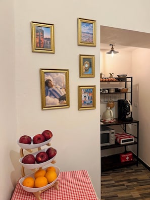 A room with a wall decorated with framed pictures, a table with a checkered tablecloth, and a shelf with kitchen appliances.