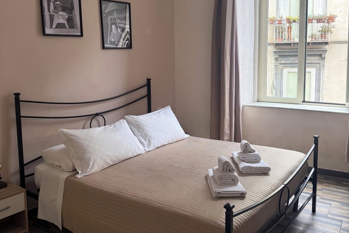 A bedroom with a bed, two framed pictures, a window with curtains, and a wooden floor.
