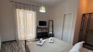 Hotellihuone, jossa on sänky, työpöytä, televisio, peili ja vaatekaappi.