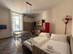 A compact room with a bed, a dining table with chairs, a kitchen area, and a window.