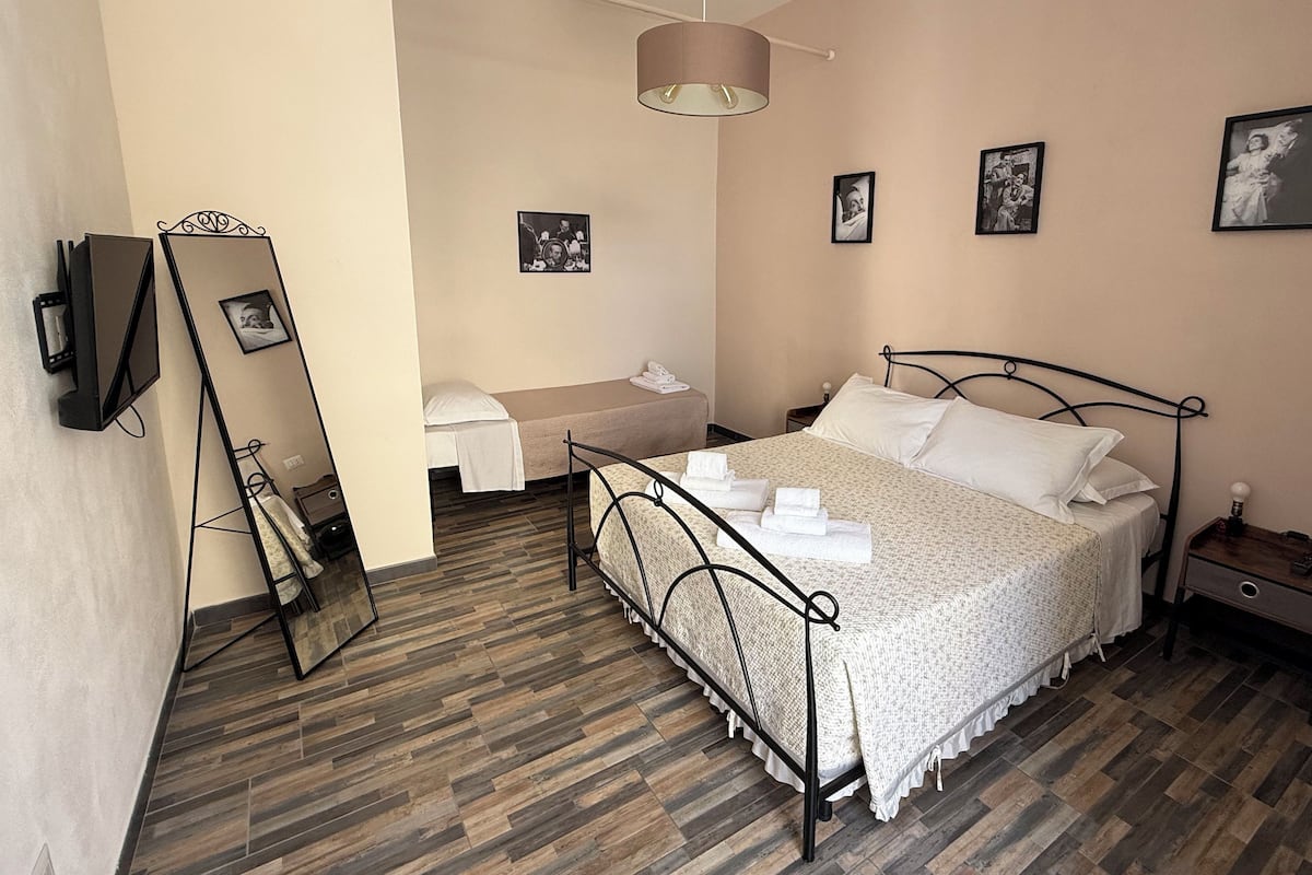 A bedroom with a bed, a bedside table, a mirror, and a wall-mounted TV.