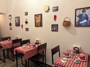 A dining area with checkered tablecloths, chairs, and framed pictures on the wall.