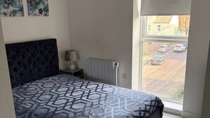 A bedroom with a large bed, a radiator, a lamp, and a window with a view of the street. - Pristine & Cozy 3 bed 2 Bath Apartment in a Great Location (Coventry)