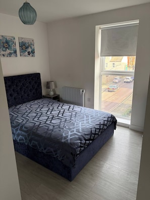 A bedroom with a large bed, a radiator, a lamp, and a window with a view of the street. - Pristine & Cozy 3 bed 2 Bath Apartment in a Great Location (Coventry)