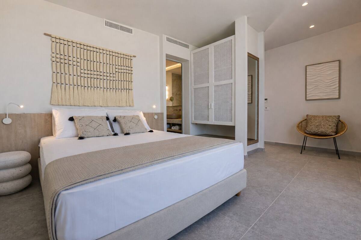 A modern bedroom with a large bed, a woven headboard, a wicker chair, and a built-in wardrobe.